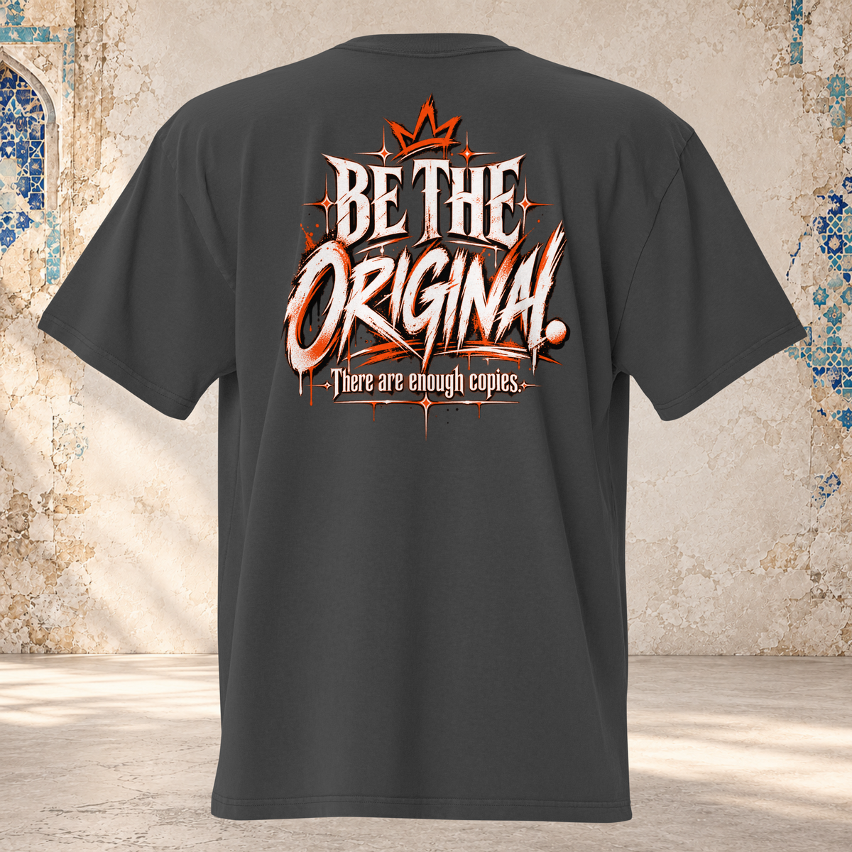Back mockup of a faded black oversized tee with a crown and cream and orange "BE THE ORIGINAL." lettering