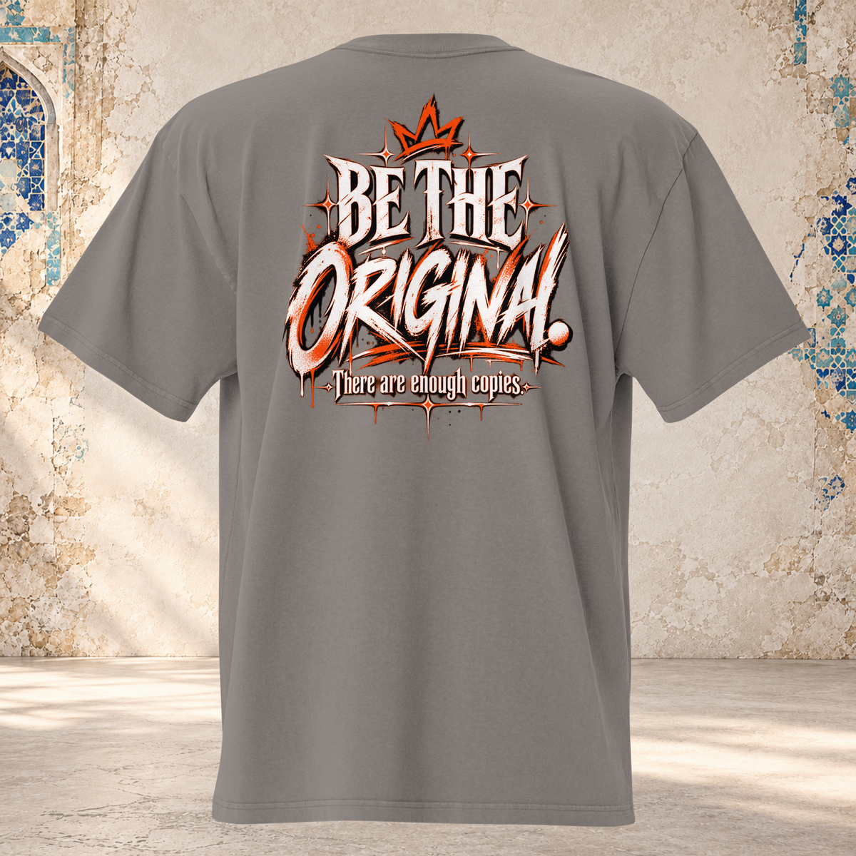 Back mockup of a faded grey oversized tee with a crown and cream and orange "BE THE ORIGINAL." lettering