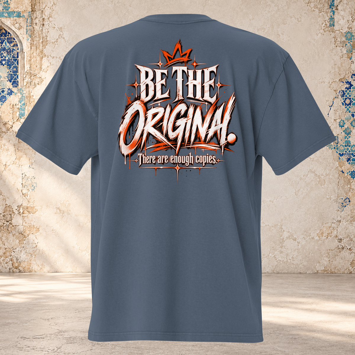 Back mockup of a faded indigo oversized tee with a crown and cream and orange "BE THE ORIGINAL." lettering