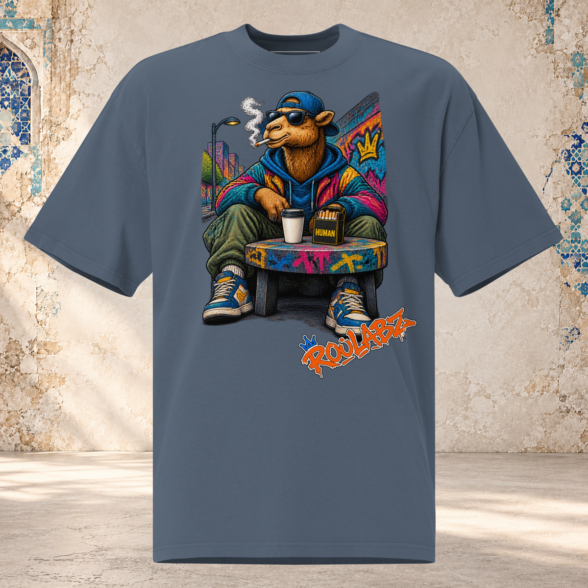 Front mockup of a faded indigo oversized tee with a camel in sunglasses and a blue cap seated on a graffiti-covered chair