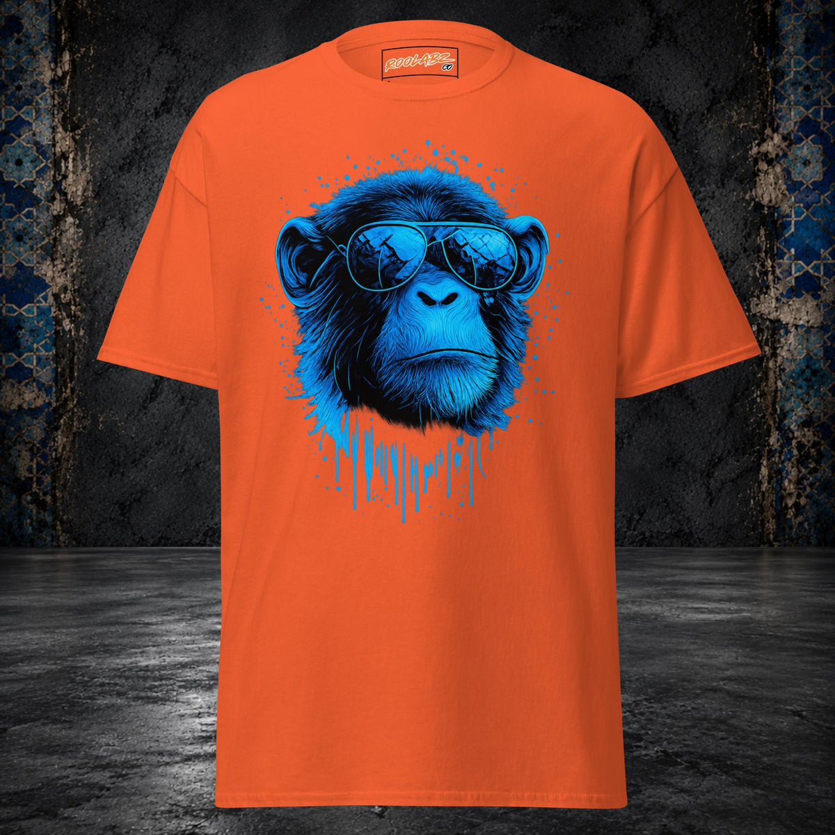 Front mockup of a orange tee with a blue monkey portrait in sunglasses framed by ink splashes and drips