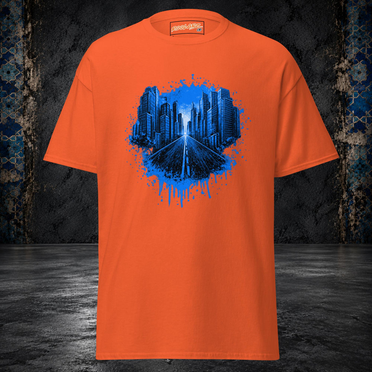 Front mockup of a orange tee with an electric-blue skyline and highway framed by paint splashes and drips