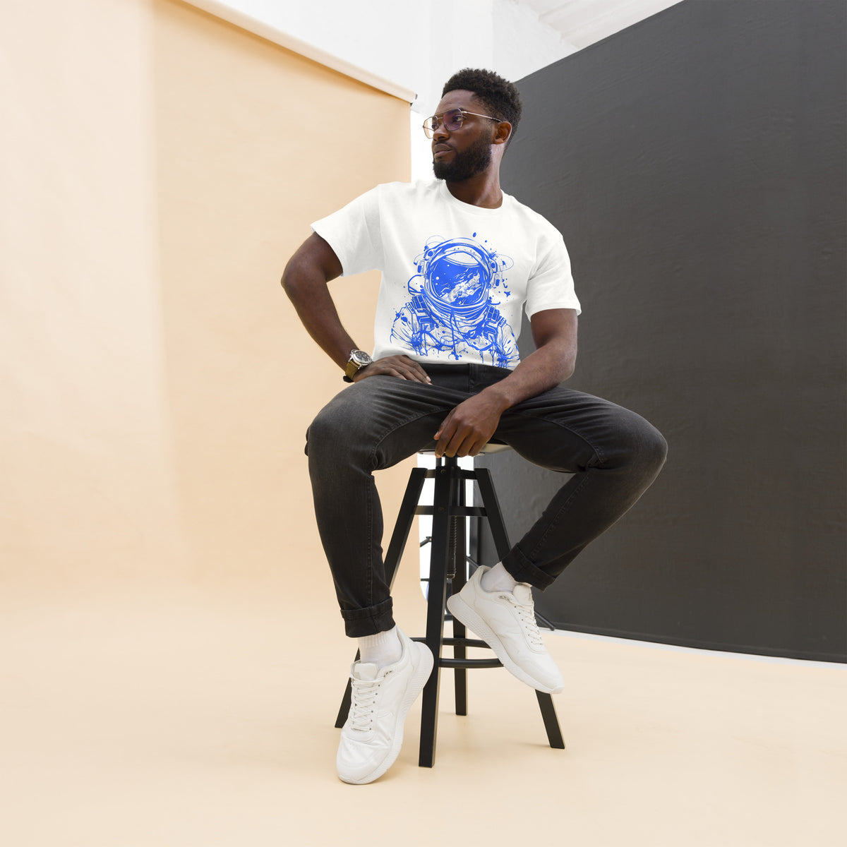 Model seated on a stool wearing a white Blue Astronaut graphic tee, dark trousers and white high-top shoes