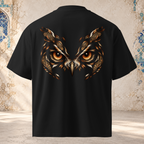 Back view of a black oversized tee showing the Owl Gaze graphic: amber eyes, copper feathers and paisley details