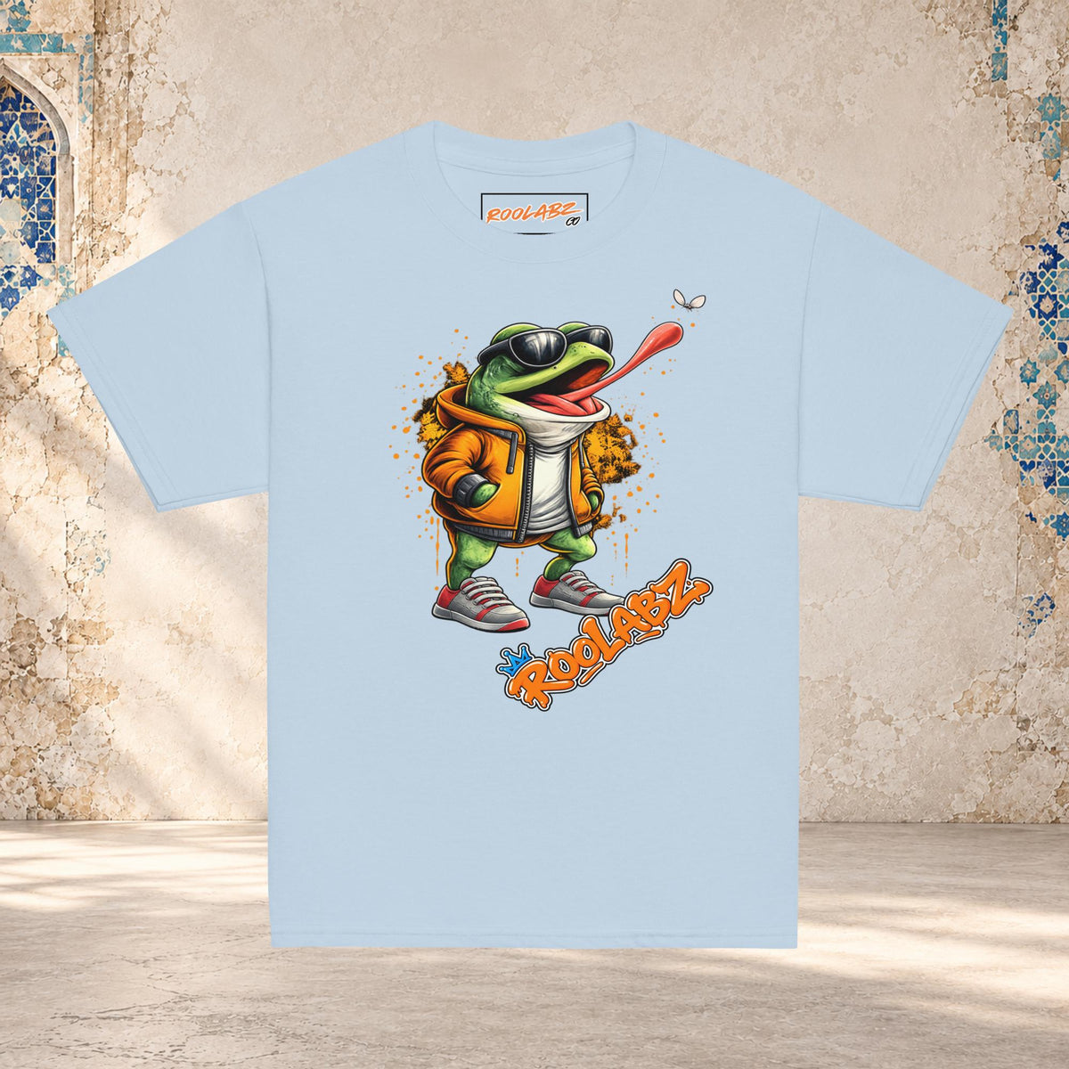 Front mockup of a light blue youth tee with a frog in sunglasses reaching its tongue toward a fly