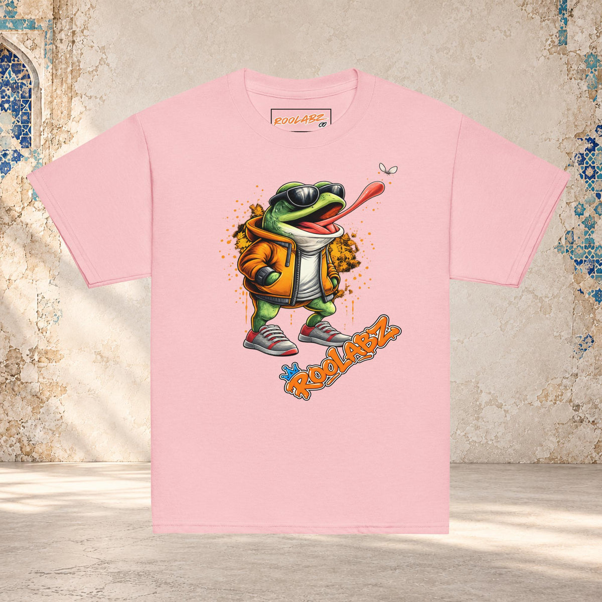 Front mockup of a light pink youth tee with a frog in sunglasses reaching its tongue toward a fly